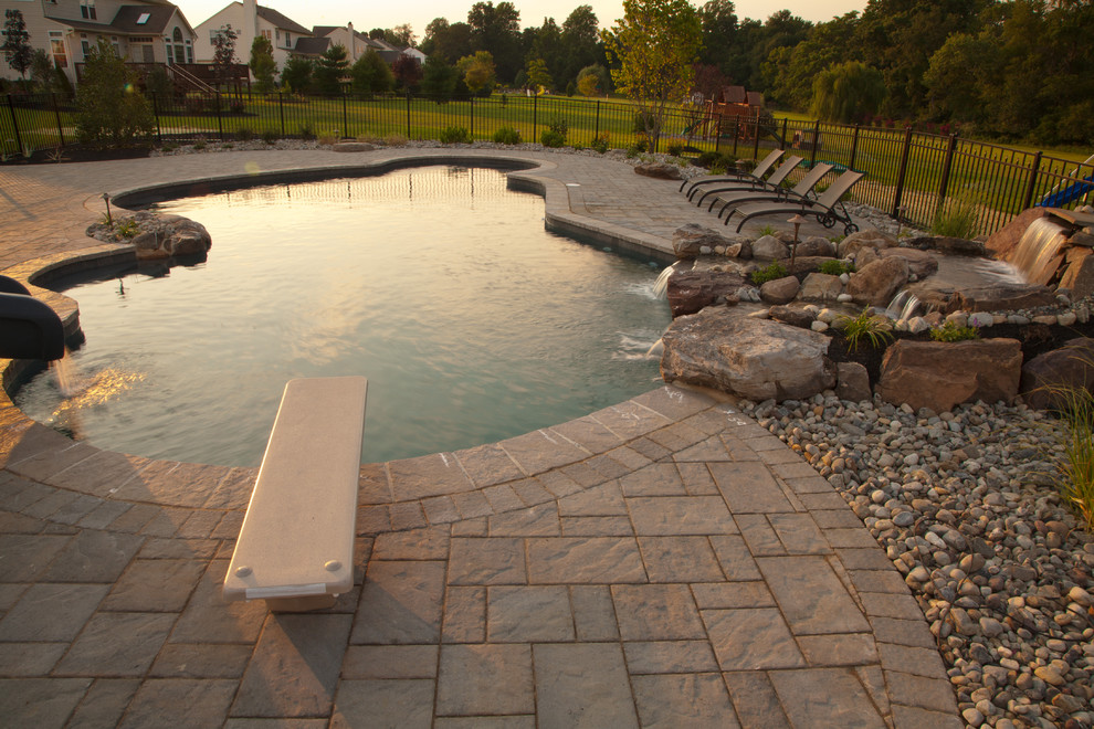 Design ideas for a large modern back custom shaped lengths swimming pool in Philadelphia with a water feature and natural stone paving.
