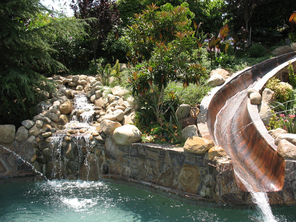 Modelo de piscina con tobogán natural mediterránea grande a medida en patio trasero con adoquines de piedra natural