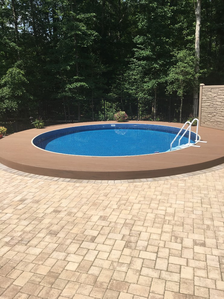 This is an example of a contemporary back round above ground swimming pool in Richmond with natural stone paving.