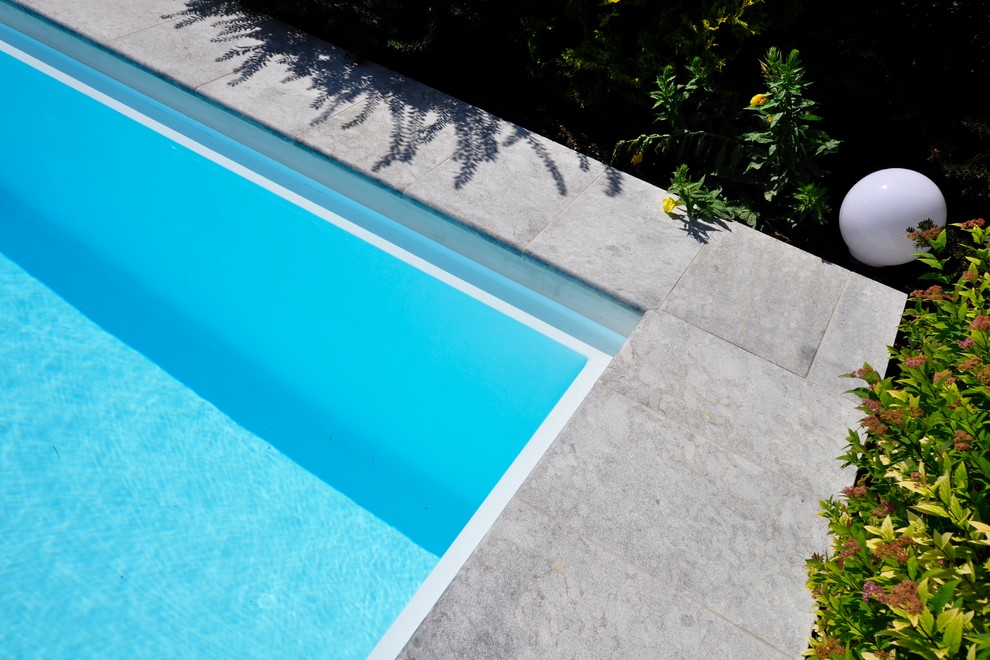 Ejemplo de piscina elevada minimalista grande rectangular en patio trasero con adoquines de piedra natural