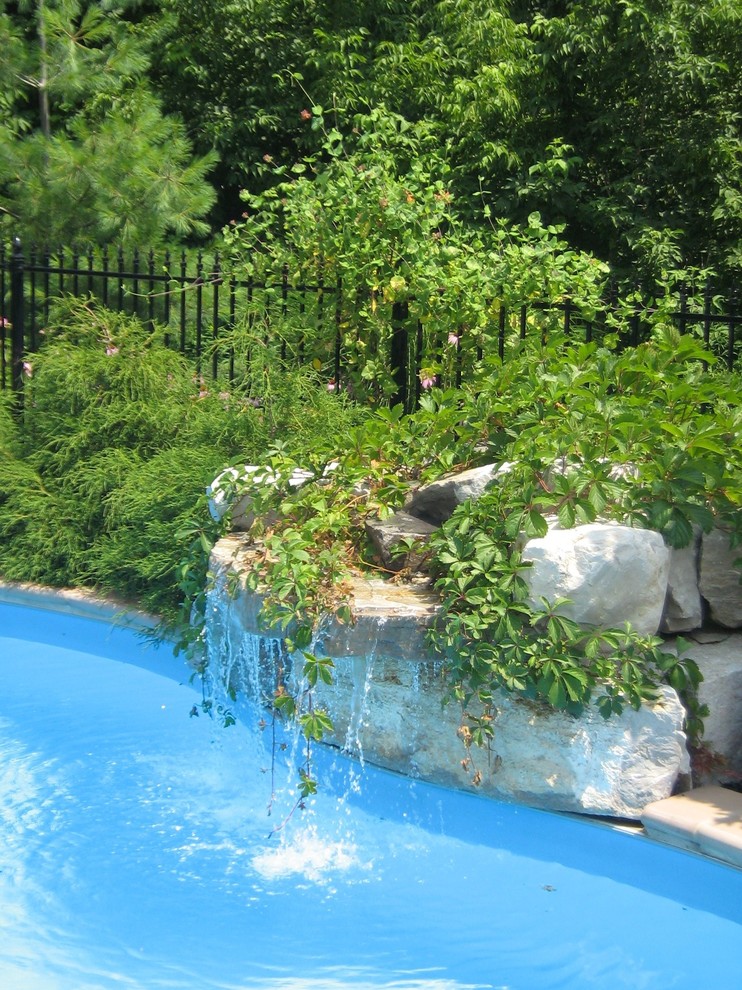 Exempel på en stor klassisk anpassad baddamm på baksidan av huset, med en fontän och naturstensplattor