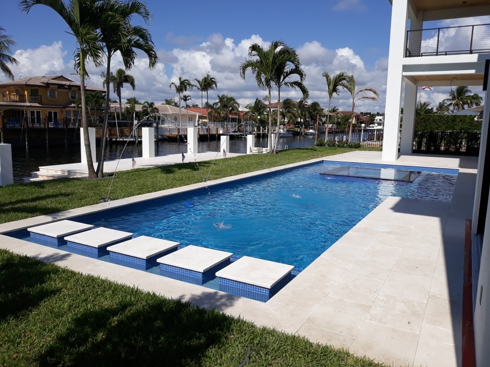 Foto di una grande piscina a sfioro infinito moderna rettangolare dietro casa con una vasca idromassaggio e lastre di cemento