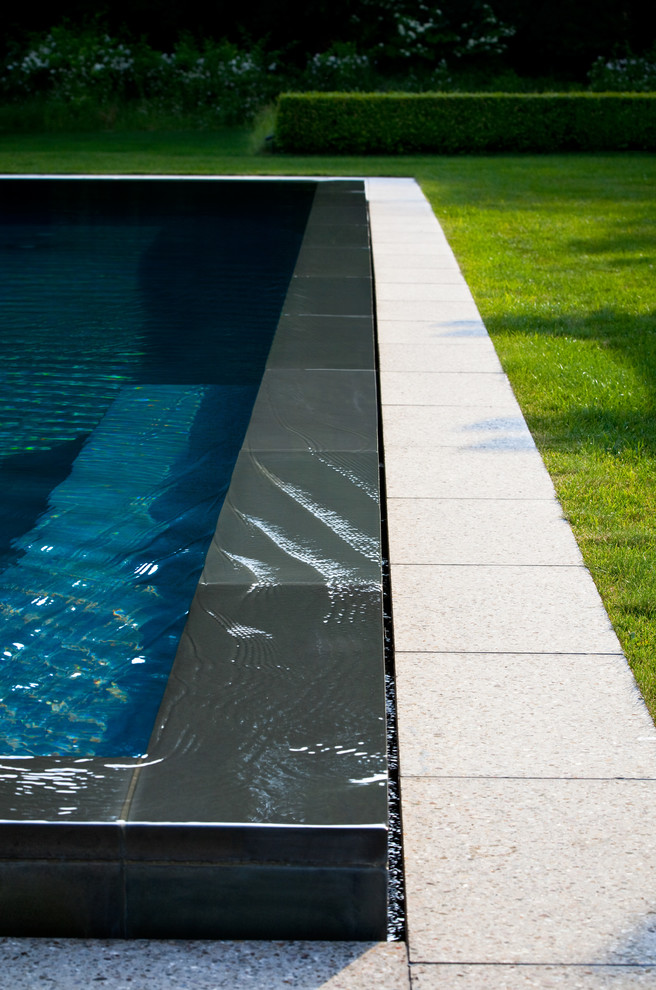 Diseño de piscina infinita moderna de tamaño medio rectangular en patio trasero con adoquines de piedra natural