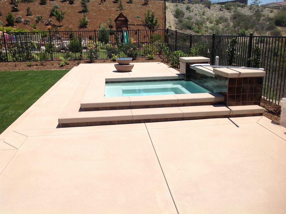 Esempio di una piccola piscina minimalista personalizzata dietro casa con una vasca idromassaggio e lastre di cemento