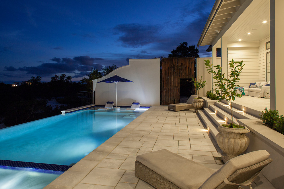 Ispirazione per una grande piscina a sfioro infinito stile marinaro rettangolare dietro casa con una vasca idromassaggio e pavimentazioni in pietra naturale