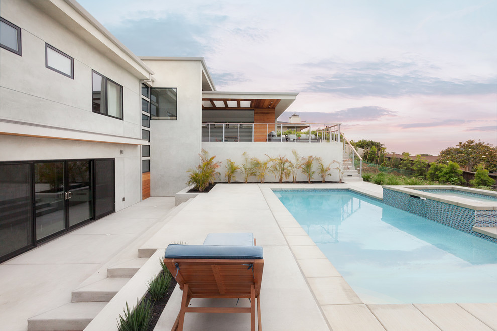 Ispirazione per una piscina monocorsia contemporanea rettangolare di medie dimensioni e dietro casa con una vasca idromassaggio e lastre di cemento