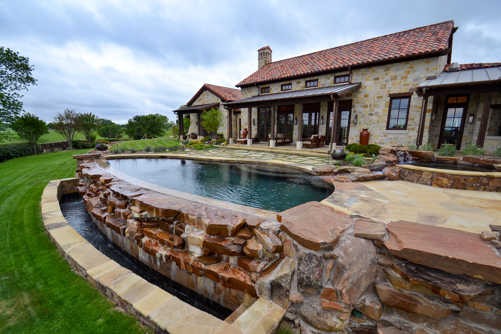 Inspiration for a medium sized rustic back custom shaped infinity swimming pool in Dallas with a water feature and natural stone paving.