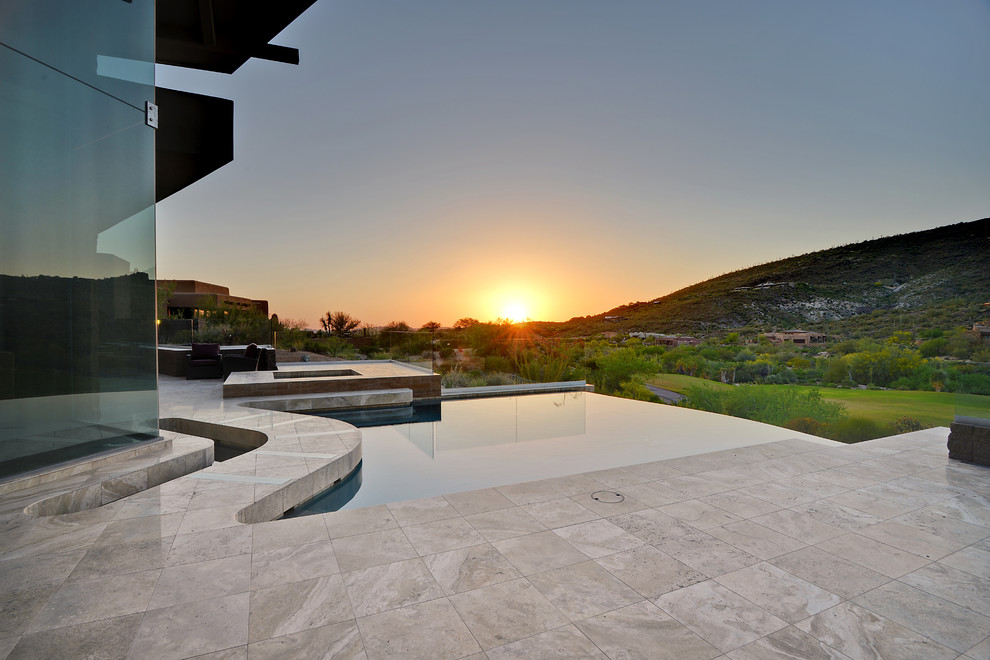 Ejemplo de piscina con fuente infinita actual de tamaño medio a medida en patio trasero con adoquines de piedra natural