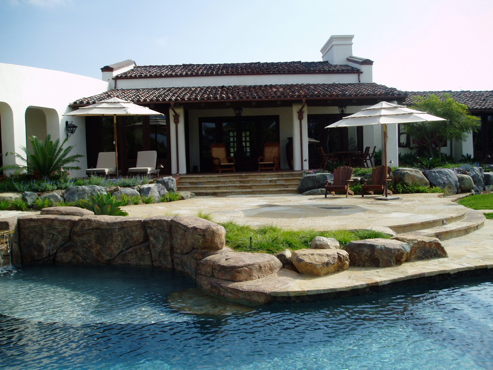 Idée de décoration pour une grande piscine arrière méditerranéenne avec un bain bouillonnant et des pavés en pierre naturelle.