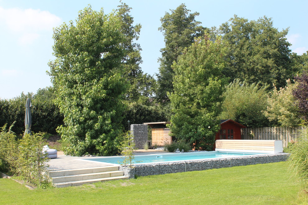 Ejemplo de casa de la piscina y piscina actual de tamaño medio rectangular en patio trasero con losas de hormigón