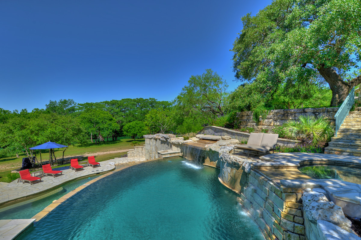 Cette photo montre une grande piscine à débordement et arrière exotique sur mesure avec un bain bouillonnant et des pavés en pierre naturelle.