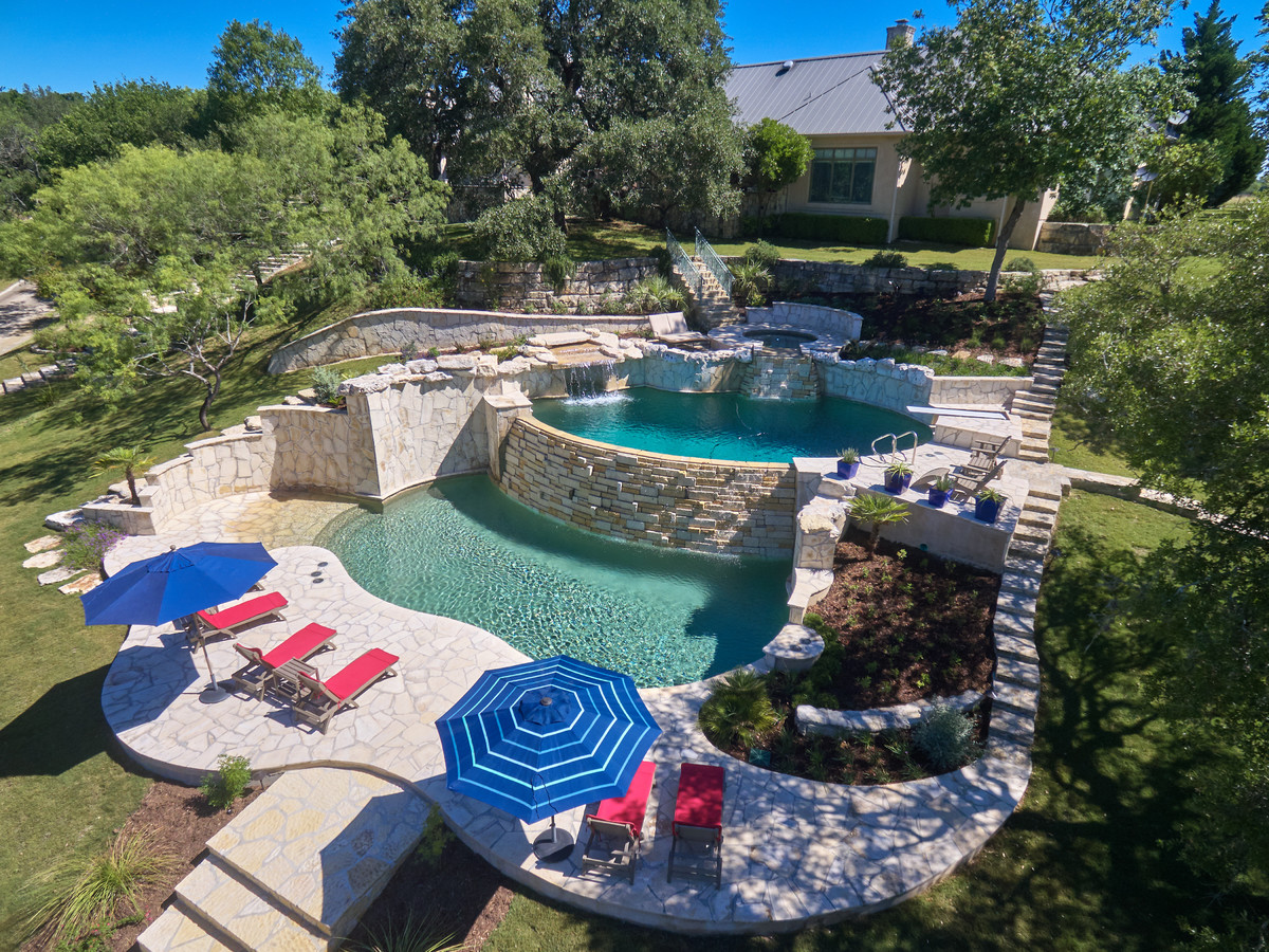 Large island style backyard custom-shaped and stone infinity hot tub photo in Austin