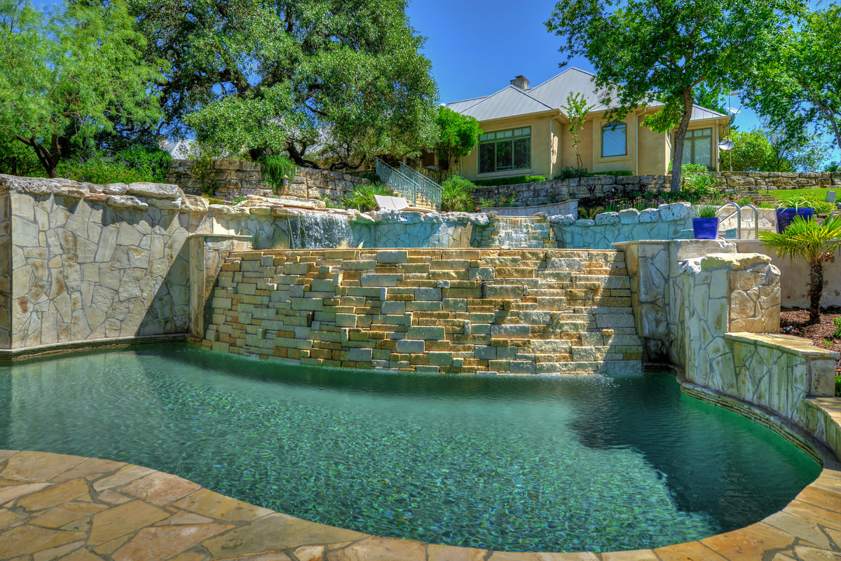Modelo de piscinas y jacuzzis infinitos tropicales grandes a medida en patio trasero con adoquines de piedra natural