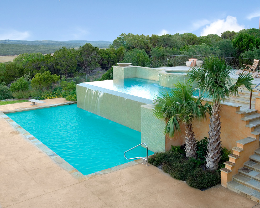 Photo of an expansive modern back custom shaped infinity swimming pool in Austin with a water feature and concrete slabs.