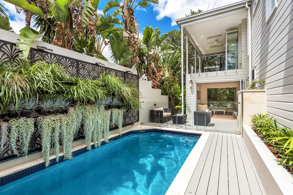 Imagen de piscina alargada tropical rectangular en patio lateral con entablado