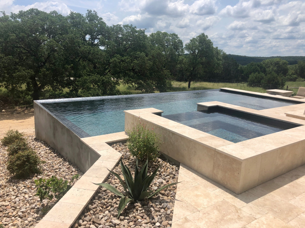Idee per un'ampia piscina a sfioro infinito moderna rettangolare dietro casa con una vasca idromassaggio e pavimentazioni in pietra naturale