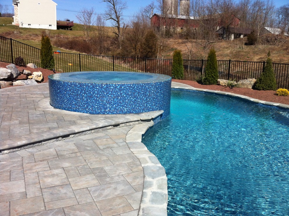 Diseño de piscina natural rústica de tamaño medio a medida en patio trasero con adoquines de hormigón