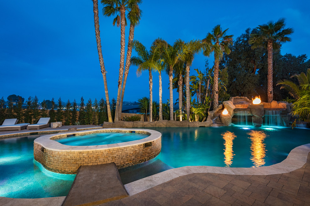 Esempio di un'ampia piscina naturale tropicale personalizzata con fontane e pavimentazioni in pietra naturale