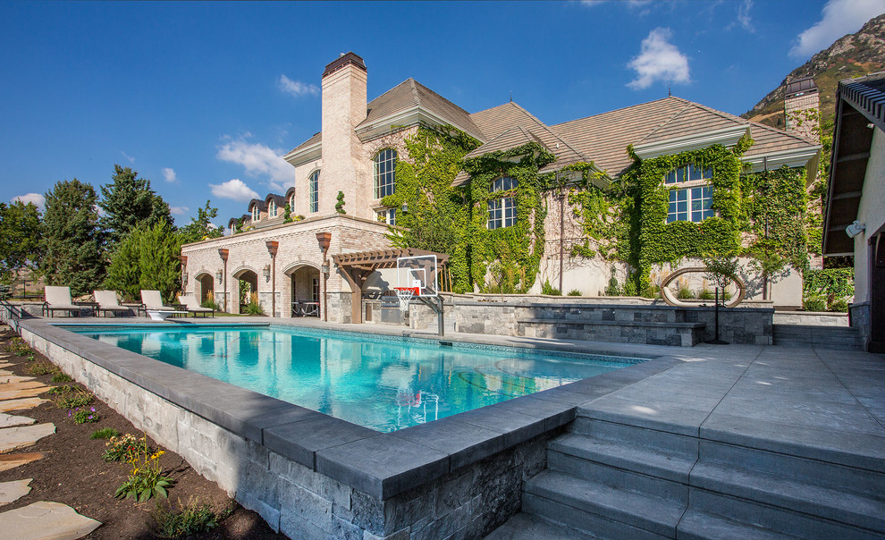 Diseño de piscina natural clásica extra grande rectangular en patio trasero con adoquines de hormigón