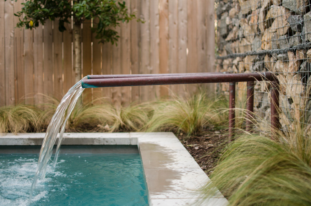 Diseño de piscina con fuente alargada industrial pequeña rectangular en patio trasero con losas de hormigón