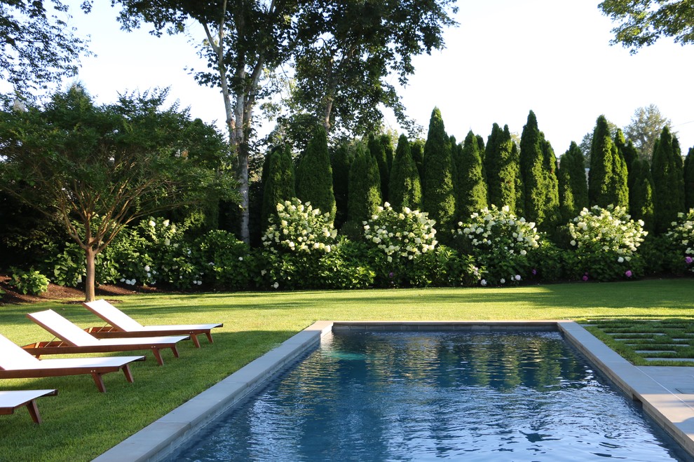 Diseño de piscina alargada tradicional rectangular en patio trasero con adoquines de piedra natural