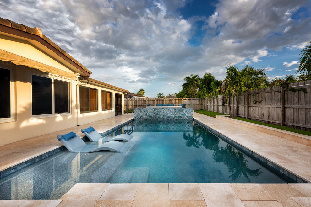 Inspiration for a medium sized modern back custom shaped infinity hot tub in Miami with natural stone paving.