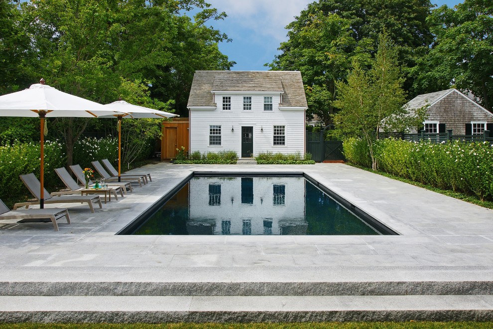 Ejemplo de piscina de estilo de casa de campo rectangular en patio trasero con adoquines de piedra natural