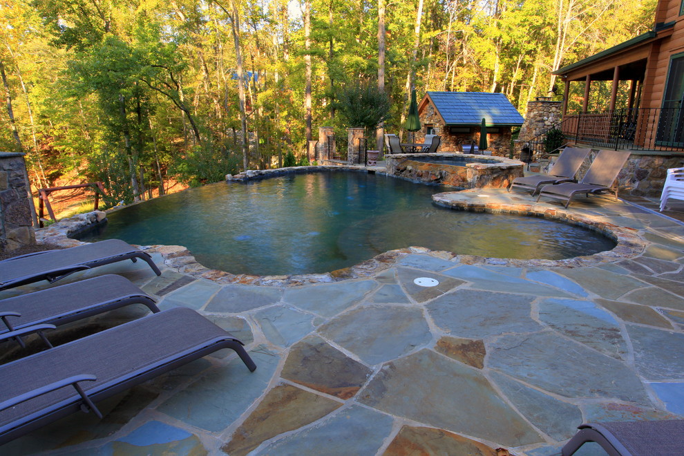 Esempio di una grande piscina a sfioro infinito rustica personalizzata dietro casa con una dépendance a bordo piscina e pavimentazioni in pietra naturale