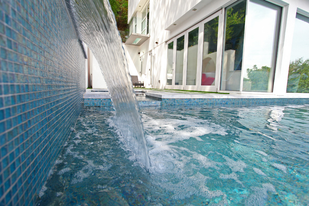Idee per una grande piscina a sfioro infinito moderna a "L" dietro casa con fontane e lastre di cemento