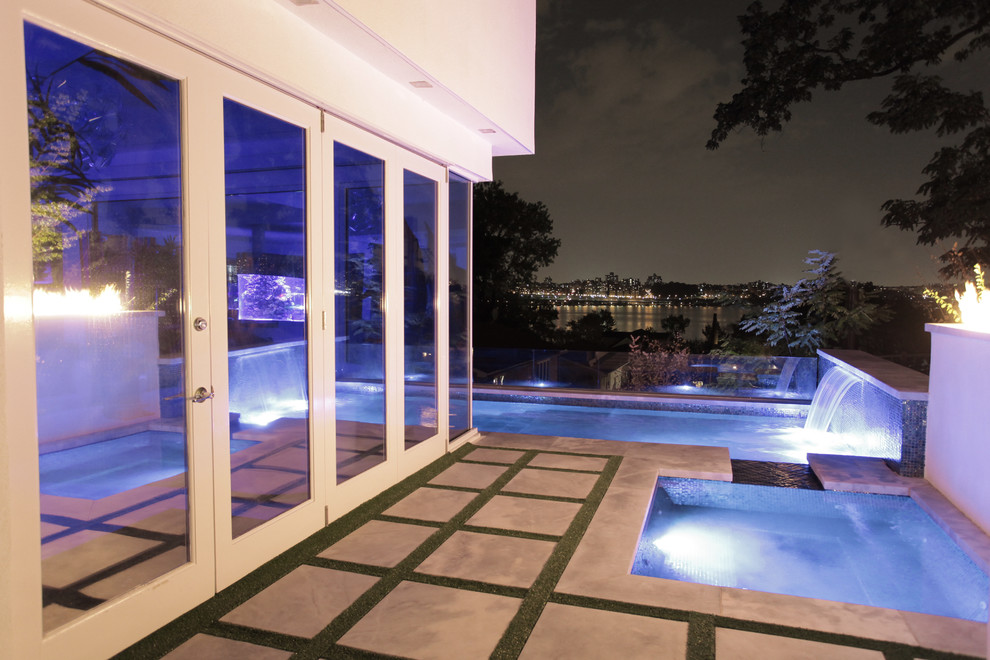 Foto de piscina con fuente infinita moderna grande en forma de L en patio lateral con losas de hormigón