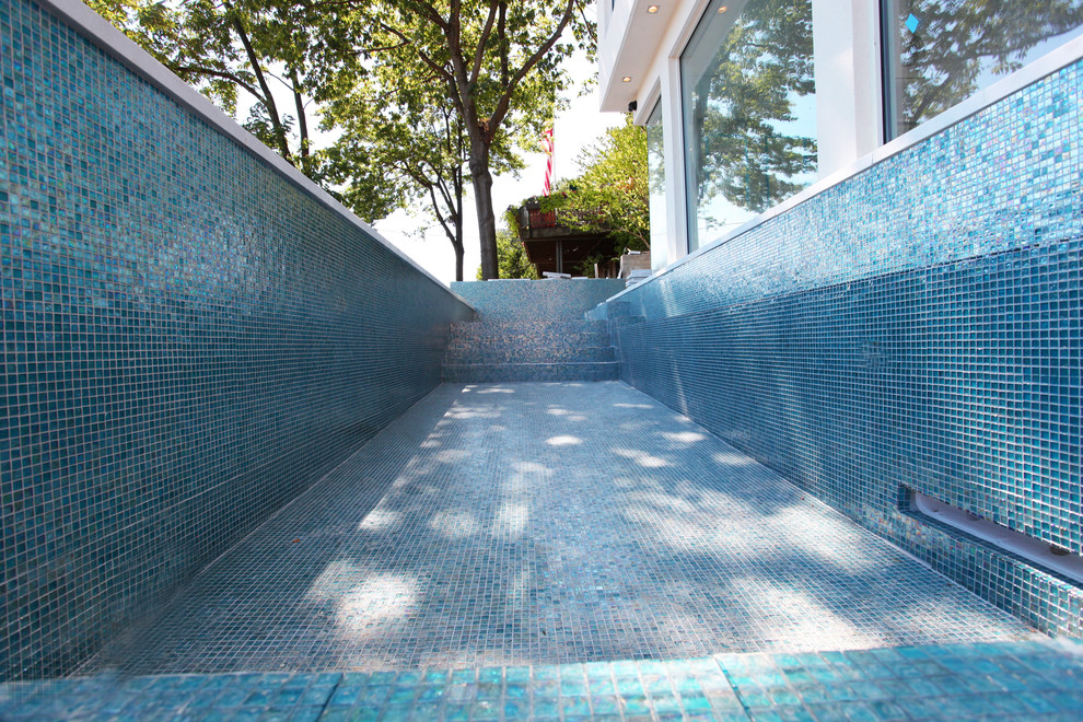 Foto de piscina con fuente alargada minimalista grande en forma de L en patio trasero con losas de hormigón