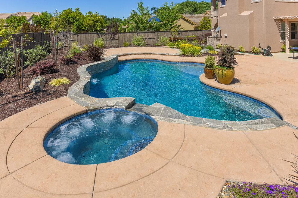 Foto di una grande piscina tropicale a "C" dietro casa con una vasca idromassaggio e pavimentazioni in pietra naturale