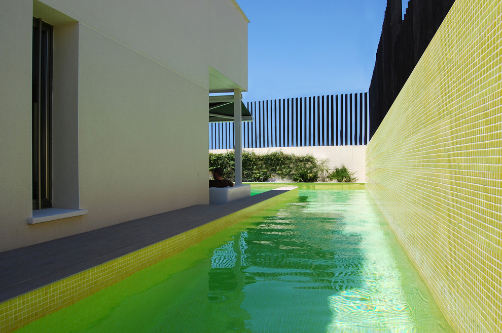 Modelo de casa de la piscina y piscina alargada contemporánea en forma de L en patio lateral con suelo de baldosas