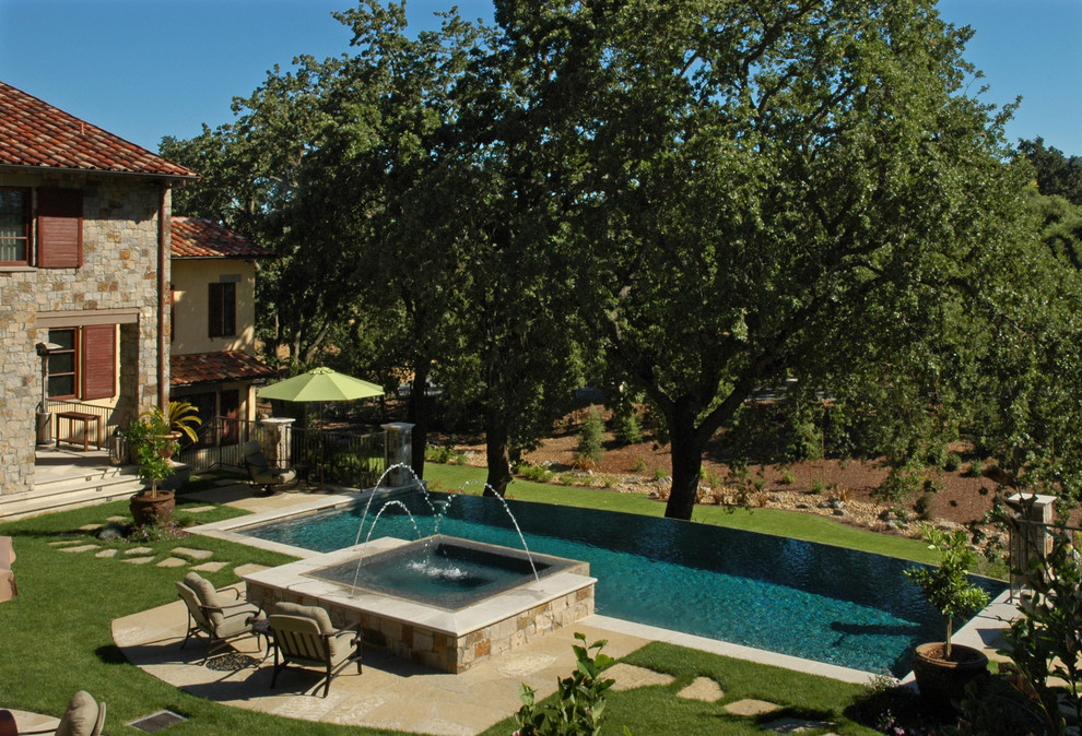 Foto di una piscina a sfioro infinito mediterranea rettangolare di medie dimensioni e dietro casa con fontane e pavimentazioni in pietra naturale
