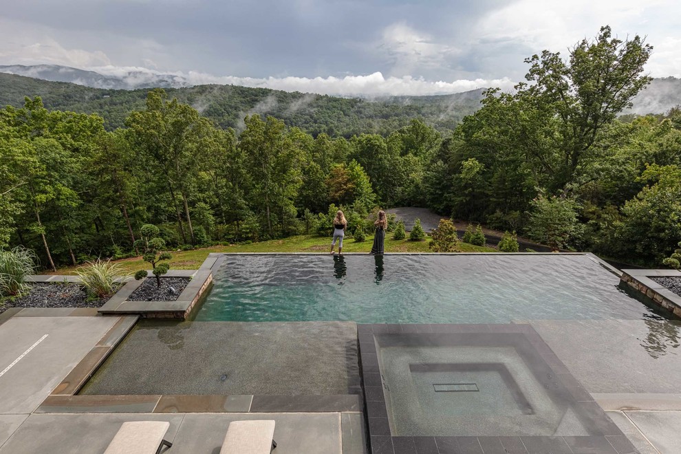 Idee per una grande piscina a sfioro infinito design rettangolare dietro casa con una vasca idromassaggio e lastre di cemento