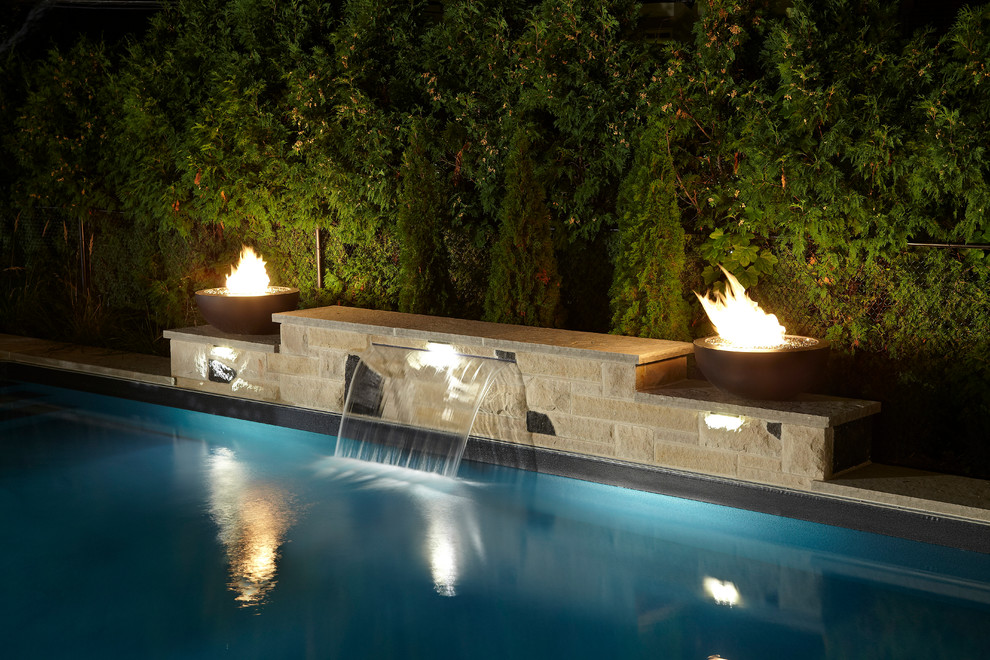 Diseño de piscina con fuente minimalista grande rectangular en patio trasero con adoquines de piedra natural