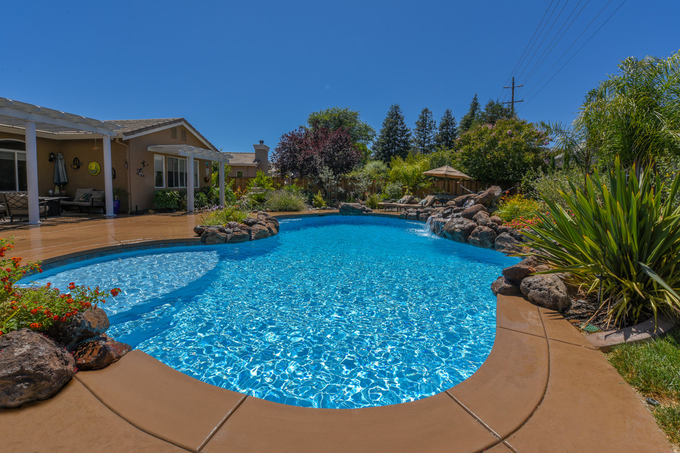 Foto di una grande piscina tropicale a "C" dietro casa con fontane e pavimentazioni in pietra naturale