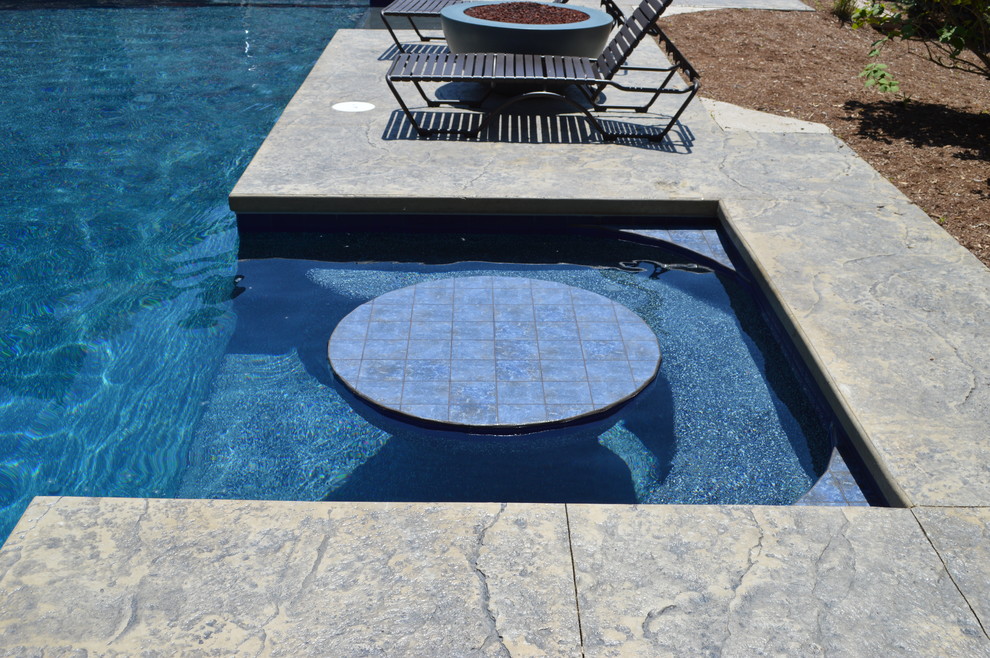 Immagine di una grande piscina design personalizzata dietro casa con una vasca idromassaggio e cemento stampato