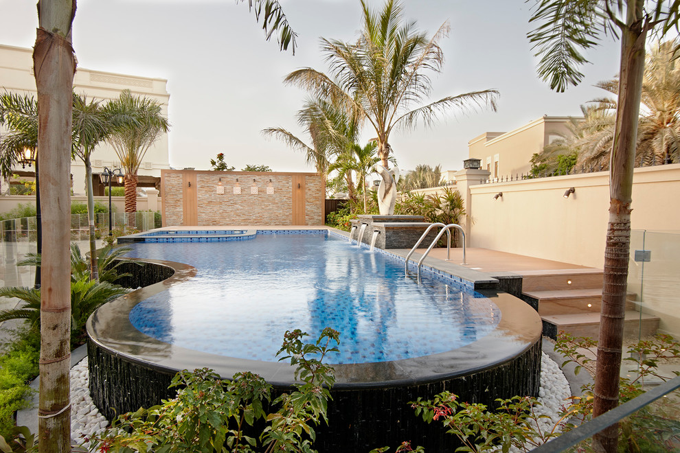 Imagen de piscina con fuente elevada mediterránea a medida en patio trasero con suelo de baldosas