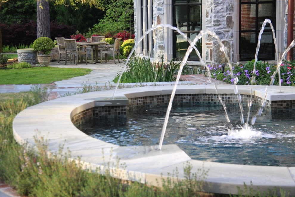 Esempio di una piscina classica personalizzata dietro casa e di medie dimensioni con pavimentazioni in pietra naturale e una vasca idromassaggio