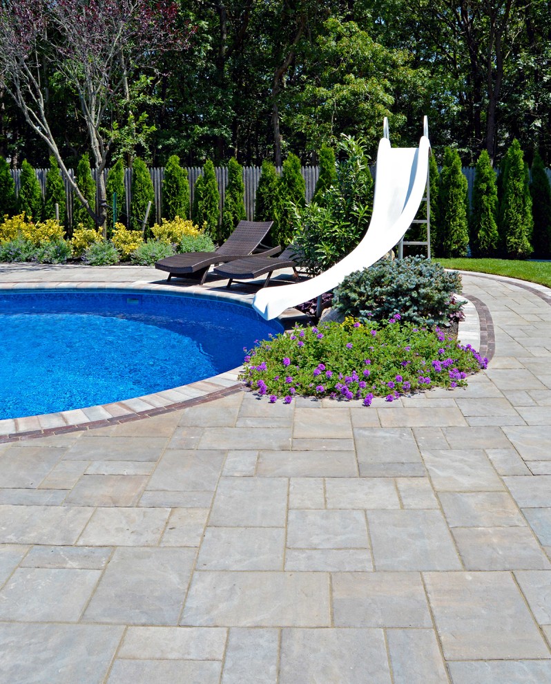 Foto de piscina con tobogán clásica tipo riñón en patio trasero con adoquines de hormigón