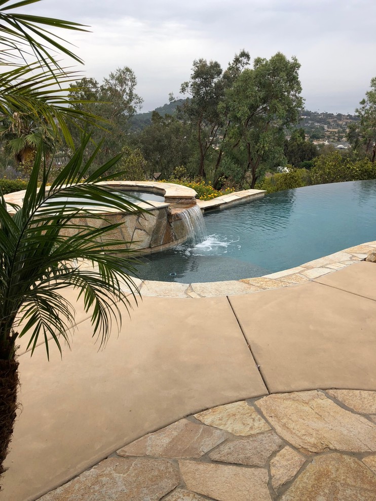 Hot tub - mid-sized tropical backyard stone and custom-shaped infinity hot tub idea in San Diego