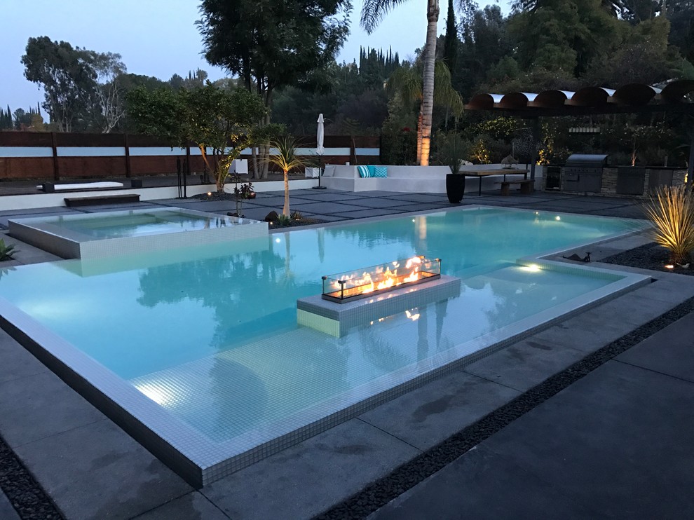 Diseño de piscina con fuente infinita moderna de tamaño medio en forma de L en patio trasero con losas de hormigón