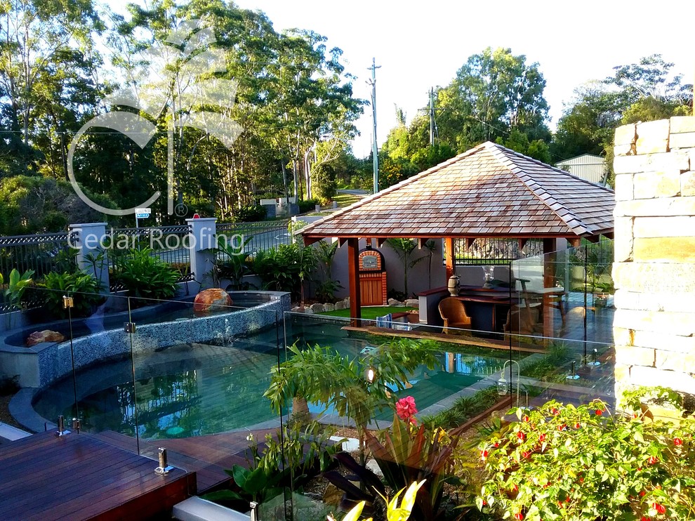 Foto de casa de la piscina y piscina natural tropical de tamaño medio a medida en patio delantero con entablado