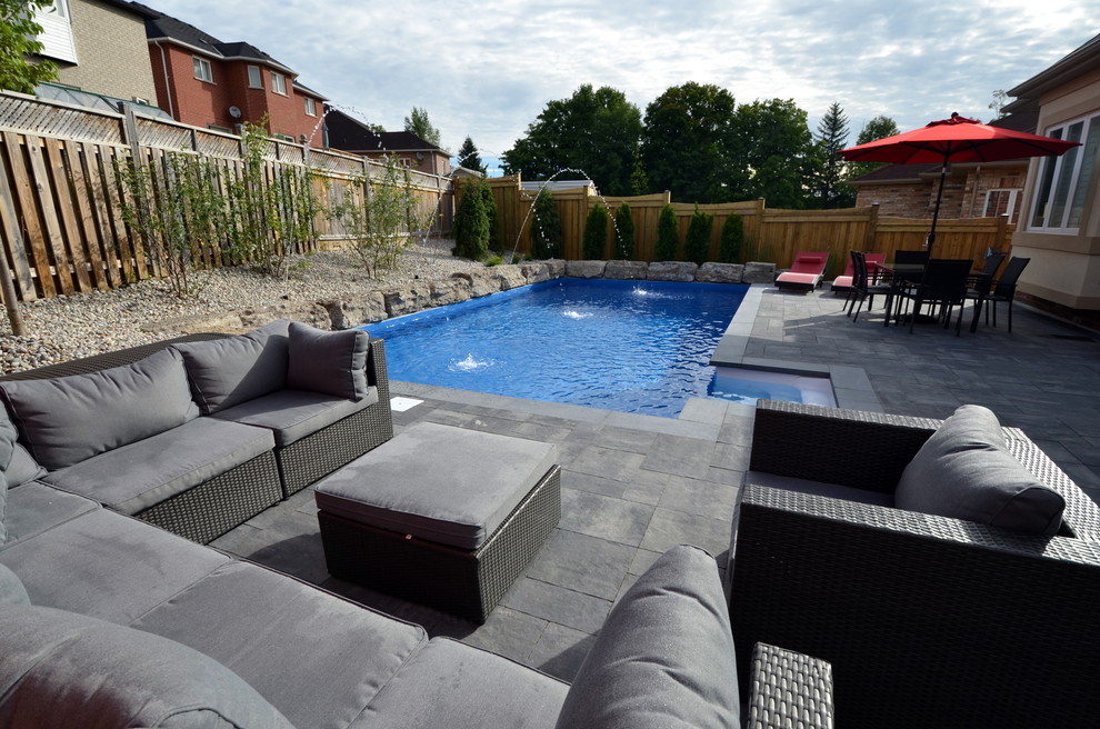 This is an example of a modern back rectangular swimming pool in Toronto with a water feature and concrete paving.