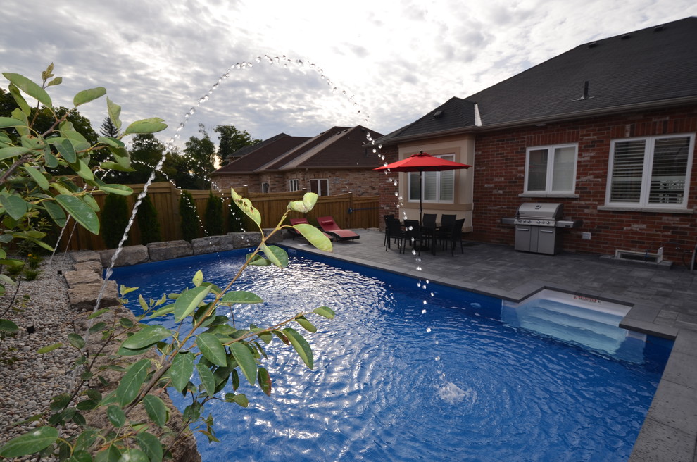 Imagen de piscina con fuente moderna rectangular en patio trasero con adoquines de hormigón
