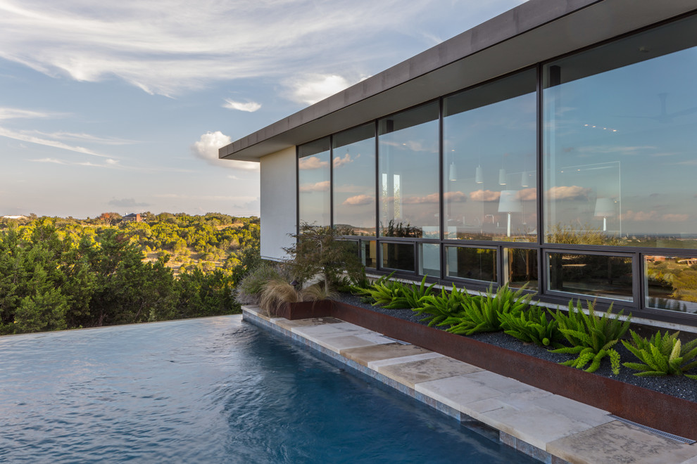 Ejemplo de piscina infinita minimalista de tamaño medio rectangular en patio lateral con adoquines de piedra natural