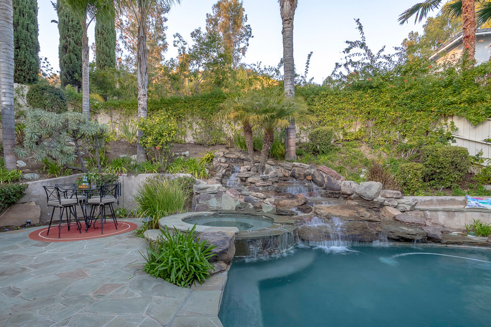 Großer Klassischer Schwimmteich hinter dem Haus in Nierenform mit Wasserspiel und Natursteinplatten in Los Angeles