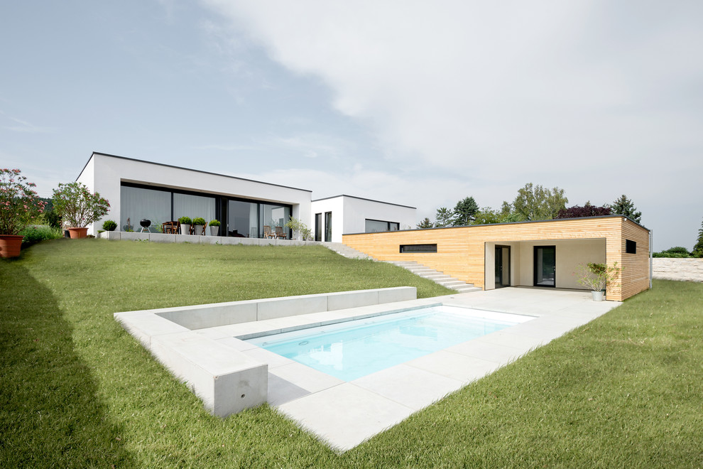 Diseño de piscina minimalista de tamaño medio rectangular en patio trasero con losas de hormigón