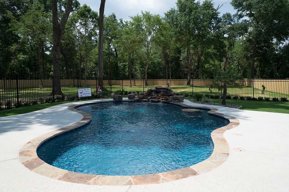 This is an example of a medium sized classic back kidney-shaped natural swimming pool in Austin with a water feature and concrete slabs.